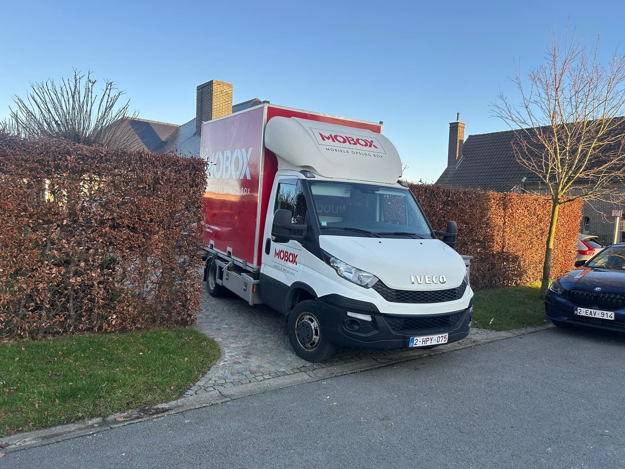 De MOBOX-bestelwagen met een box op een oprit tussen de hagen