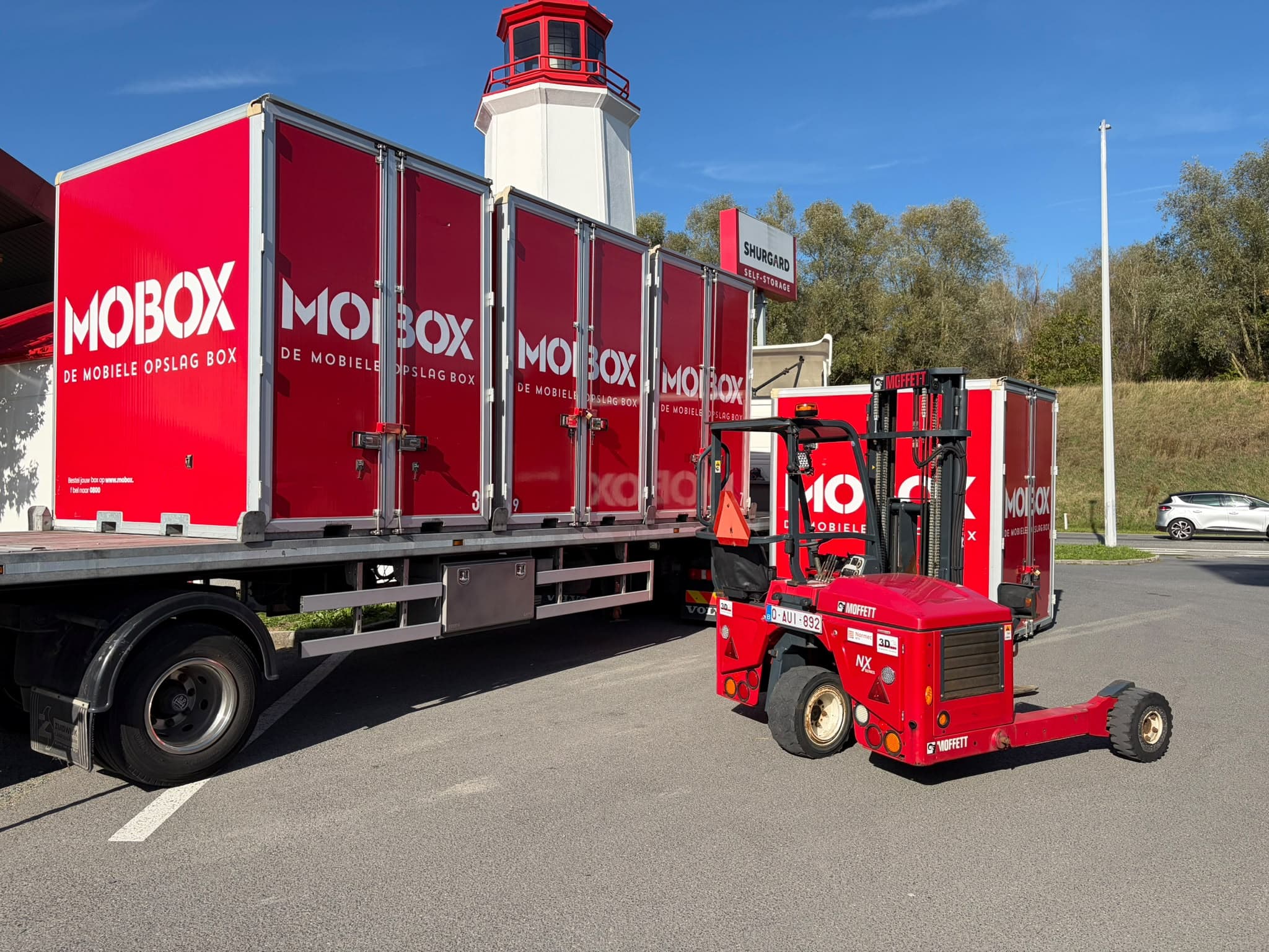 De MOBOX-vrachtwagen met boxen en heftruck aan de kust, bij de vuurtoren